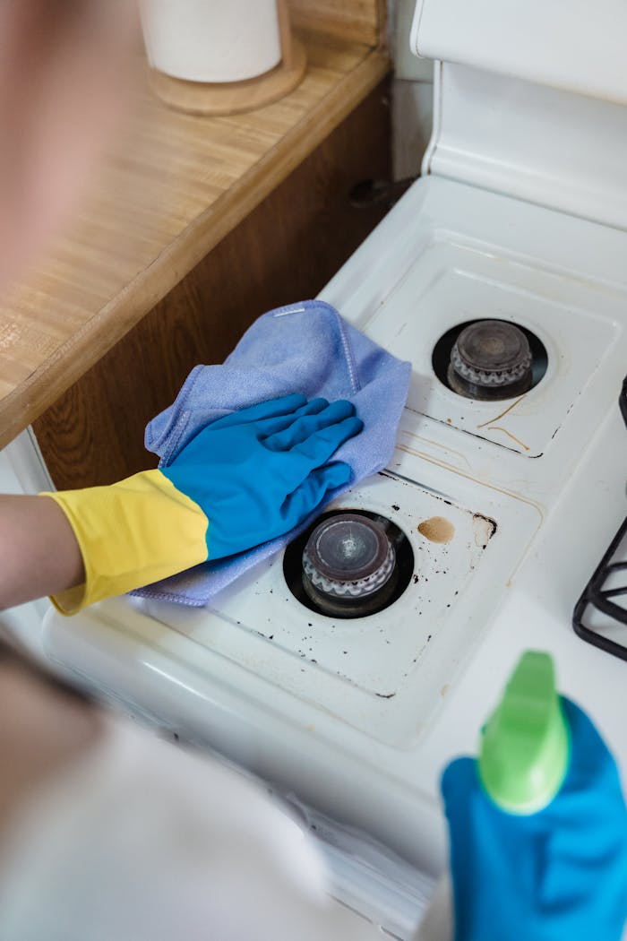 services-02 A person wearing rubber gloves cleaning a dirty gas stove with a cloth and spray bottle.